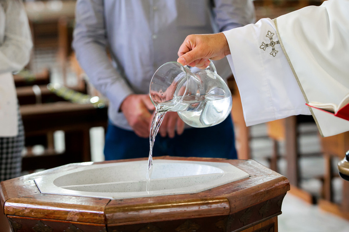 Priest pouring holy water into the baptismal font, moments before a child receives the sacrament of baptism